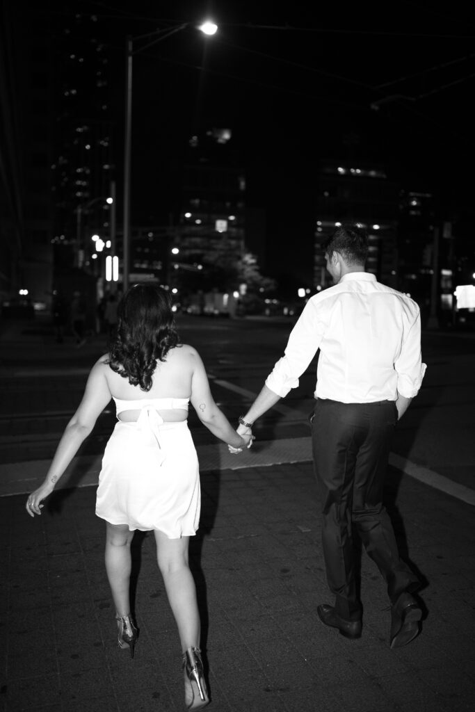 Couple walking hand-in-hand under city lights during a late-night flash engagement session