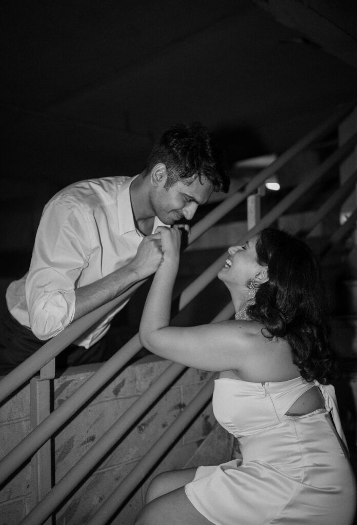 Playful couple locked in a sweet moment on a stairwell, laughing under the soft beam of flash lighting.