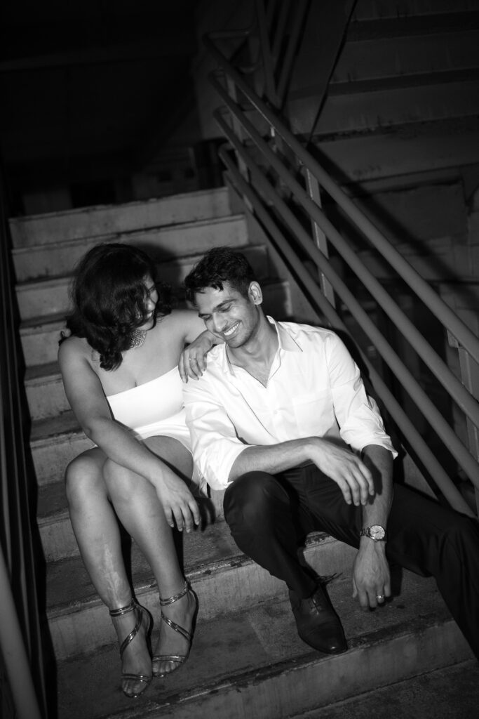 Couple sharing a candid laugh seated on concrete stairs during their night shoot