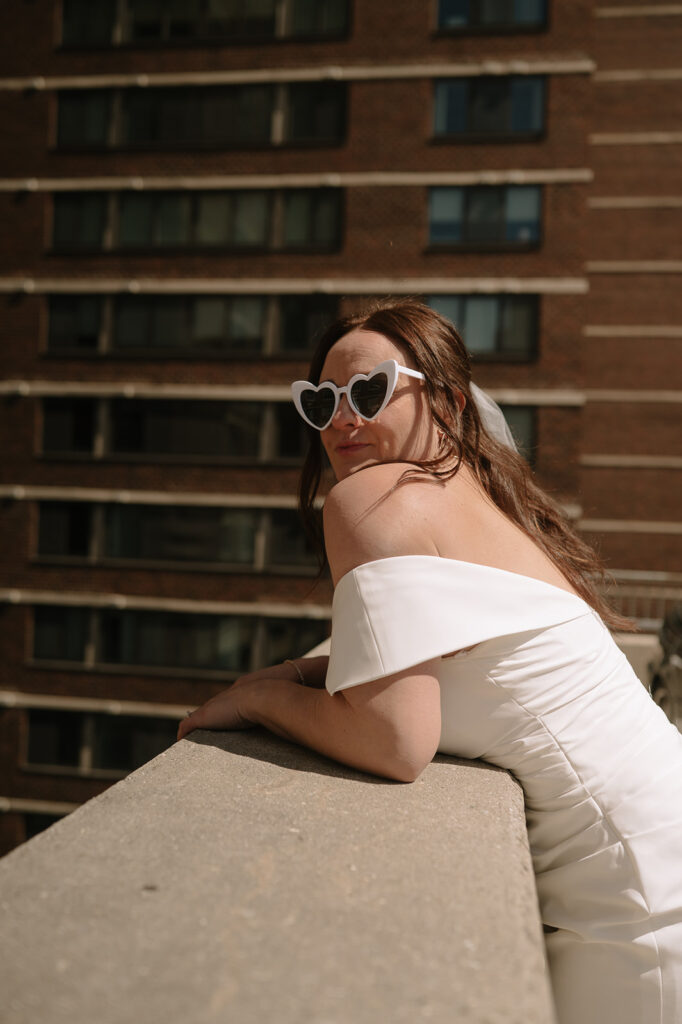 Bride wearing white heart-shaped sunglasses for her rooftop Philadelphia elopement photos