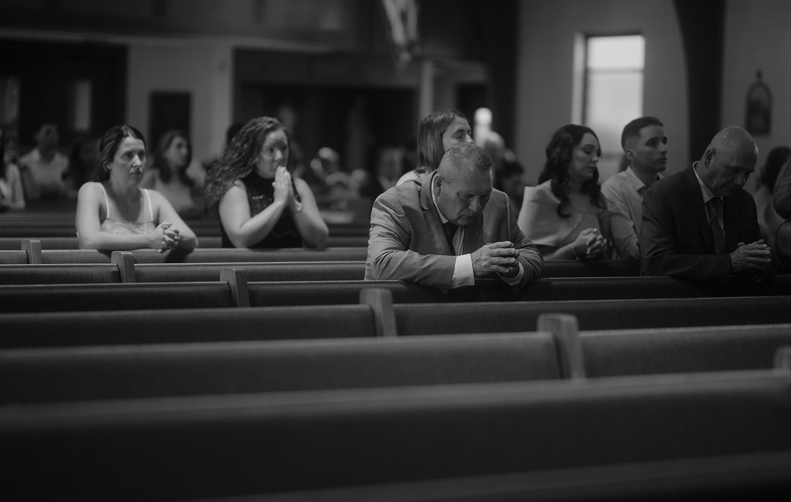 Wedding guests in pews praying during Catholic mass — storytelling wedding photography focus on faith.