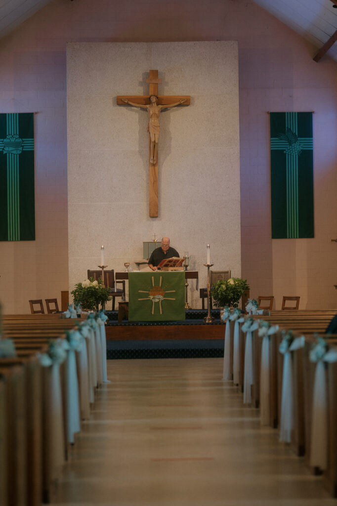 Interior of Catholic church altar with crucifix and priest preparing for mass — storytelling wedding photography of ceremony setting.