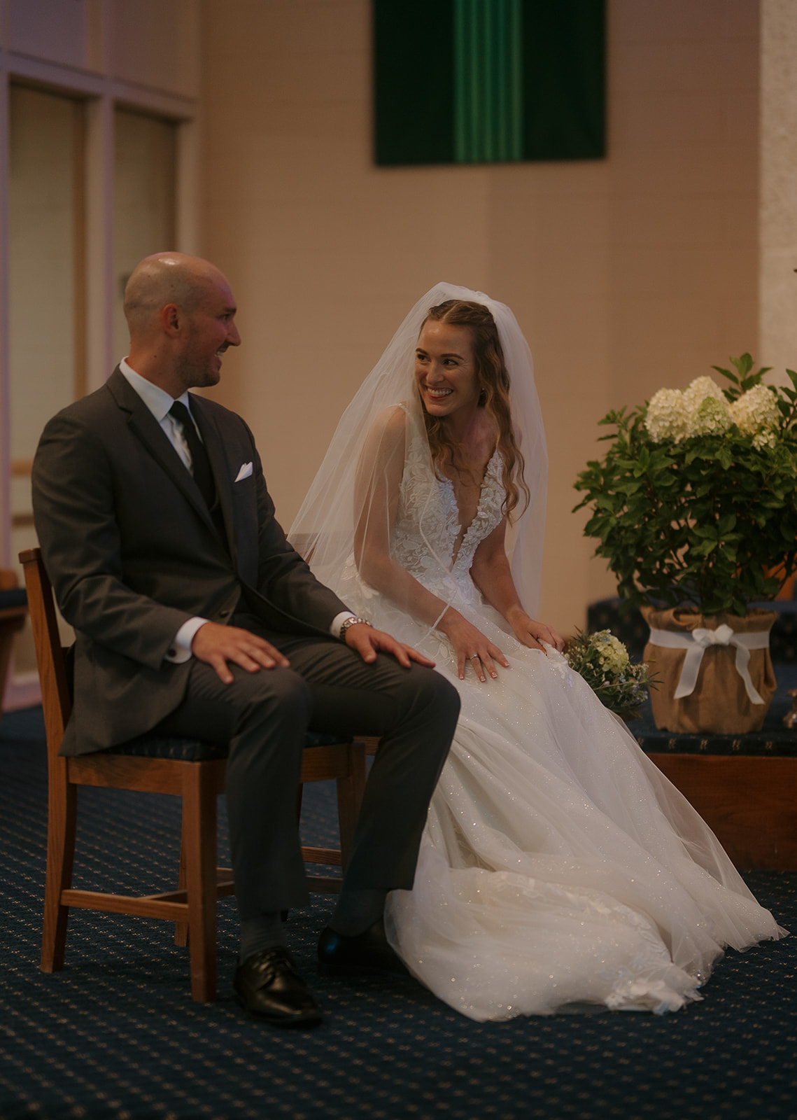 Bride and groom seated together at altar, smiling during Catholic mass — storytelling wedding photography candid joy.