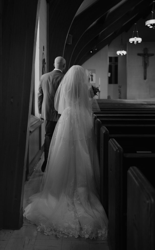 Candid black and white photo of a bride and groom walking out of the church after their Catholic wedding ceremony