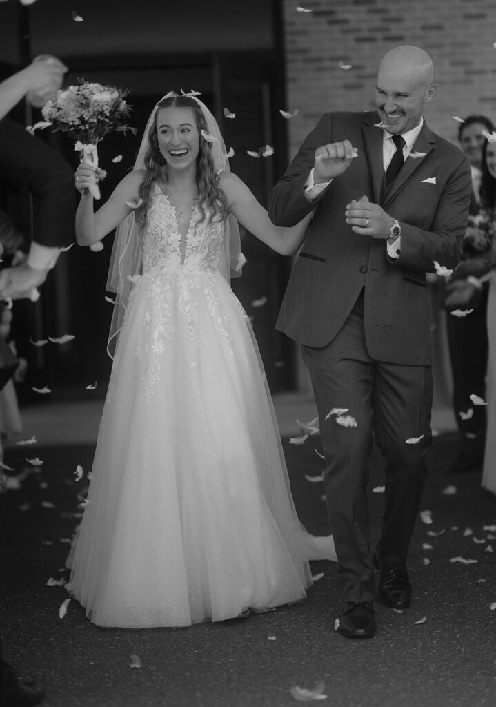 Candid black and white photo of a bride and groom walking out of the church for their wedding exit petal toss
