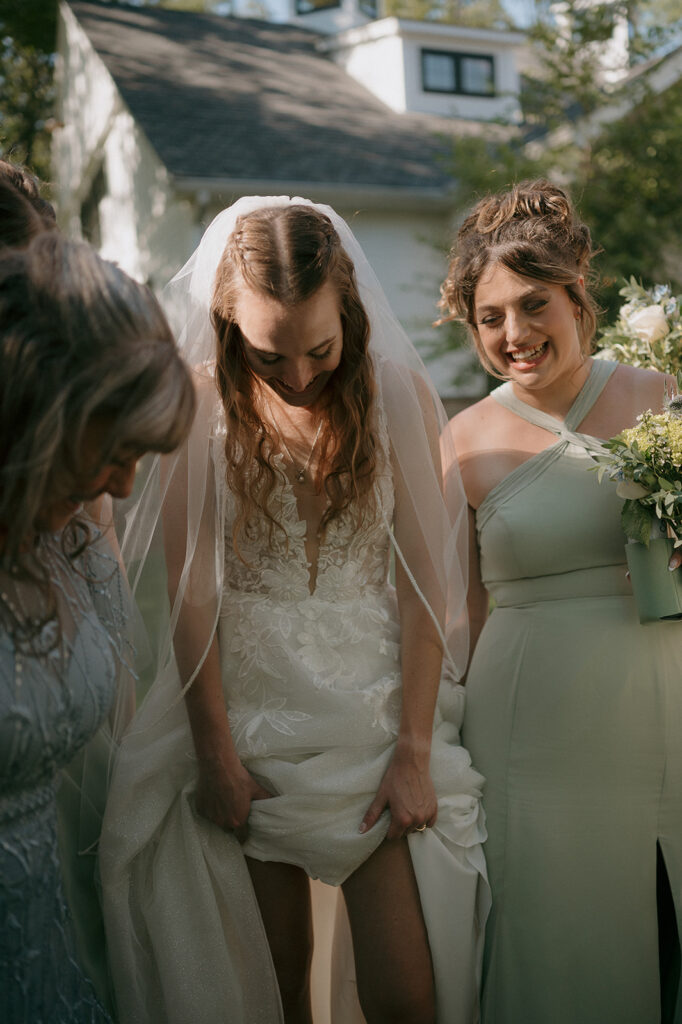 Bride smiling with bridesmaids helping her adjust dress, intimate storytelling portrait at The Inn at Millrace Pond.