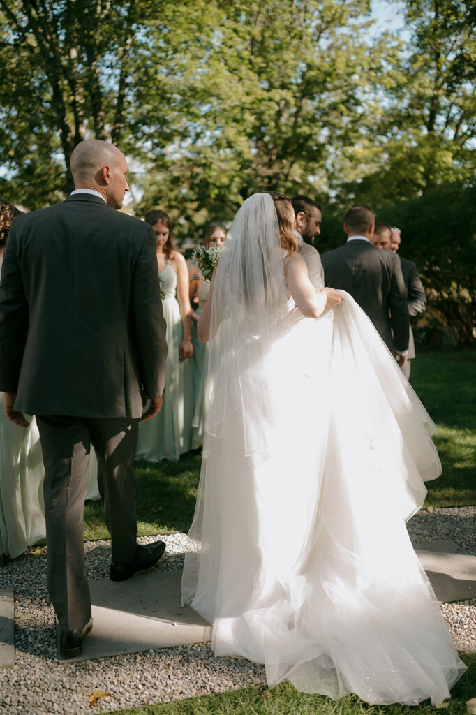 Candid photo of a bride, groom, and their wedding party waking the grounds at Millrace Pond