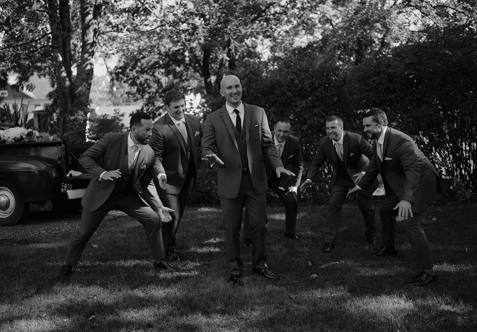 Groom laughing with groomsmen outdoors, playful candid wedding portrait at The Inn at Millrace Pond.