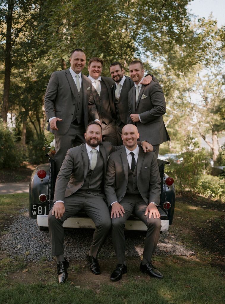 Groom smiling with groomsmen outdoors in the bed of a vintage truck at The Inn at Millrace Pond.