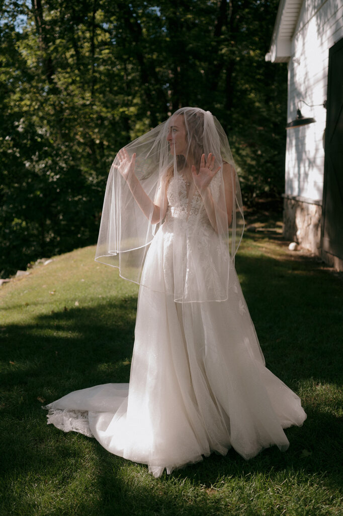 Bride in veil standing outside barn at The Inn at Millrace Pond, soft light creating timeless storytelling wedding portrait.