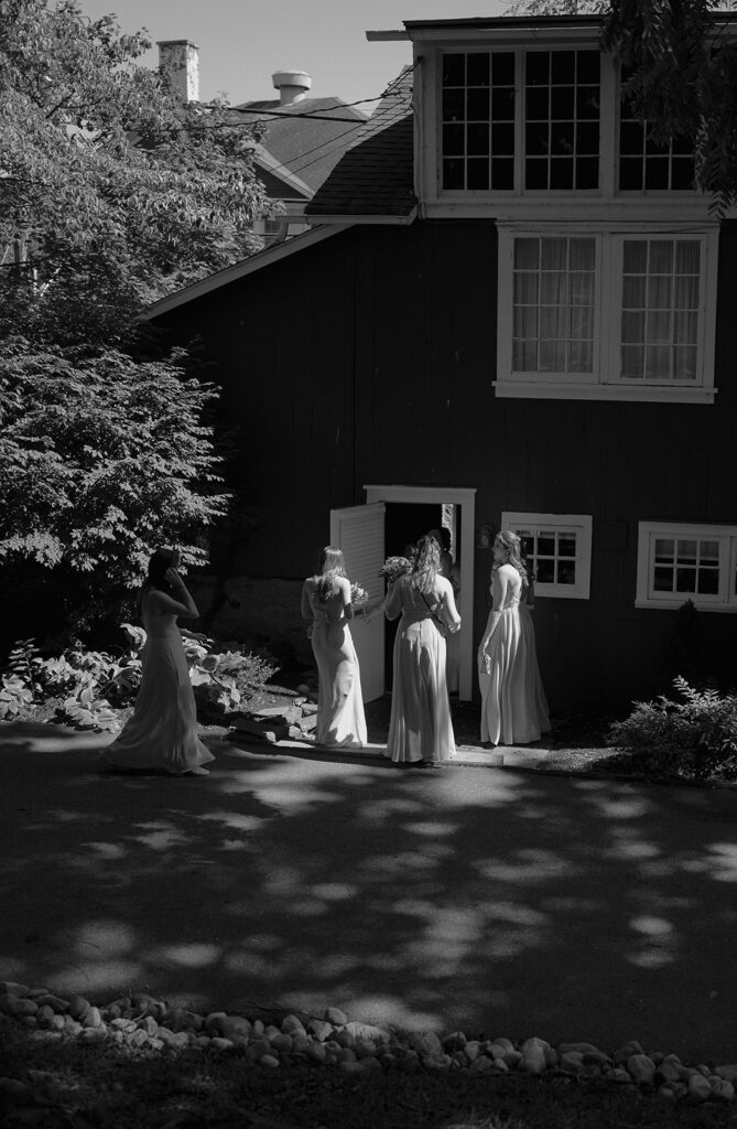 Bridesmaids in soft gowns gathered outside rustic building at The Inn at Millrace Pond — storytelling wedding photography of bridal party.