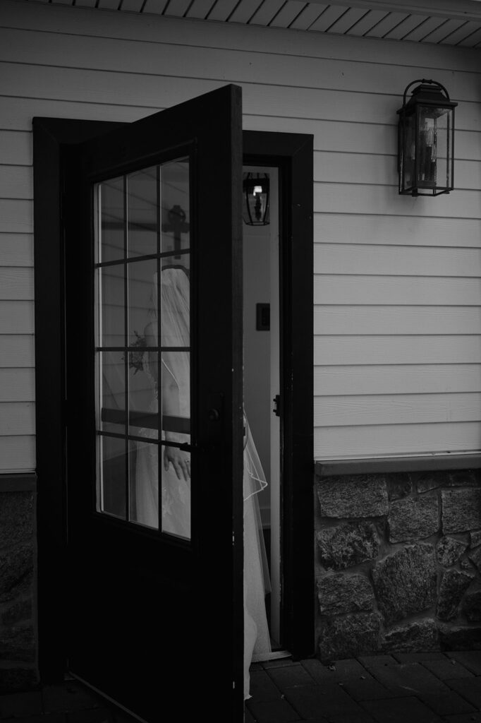 Bride captured through doorway in black and white, timeless wedding portrait at The Inn at Millrace Pond.