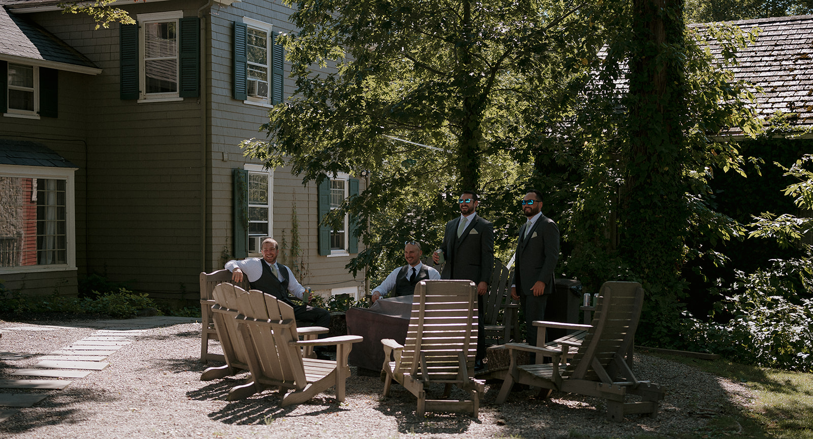 Groomsmen relaxing in Adirondack chairs outside The Inn at Millrace Pond wedding venue — candid storytelling wedding photography.