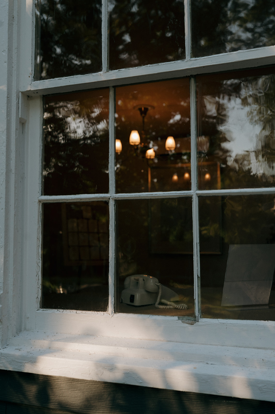 Vintage white rotary phone seen through barn window at The Inn at Millrace Pond wedding reception — storytelling wedding detail.