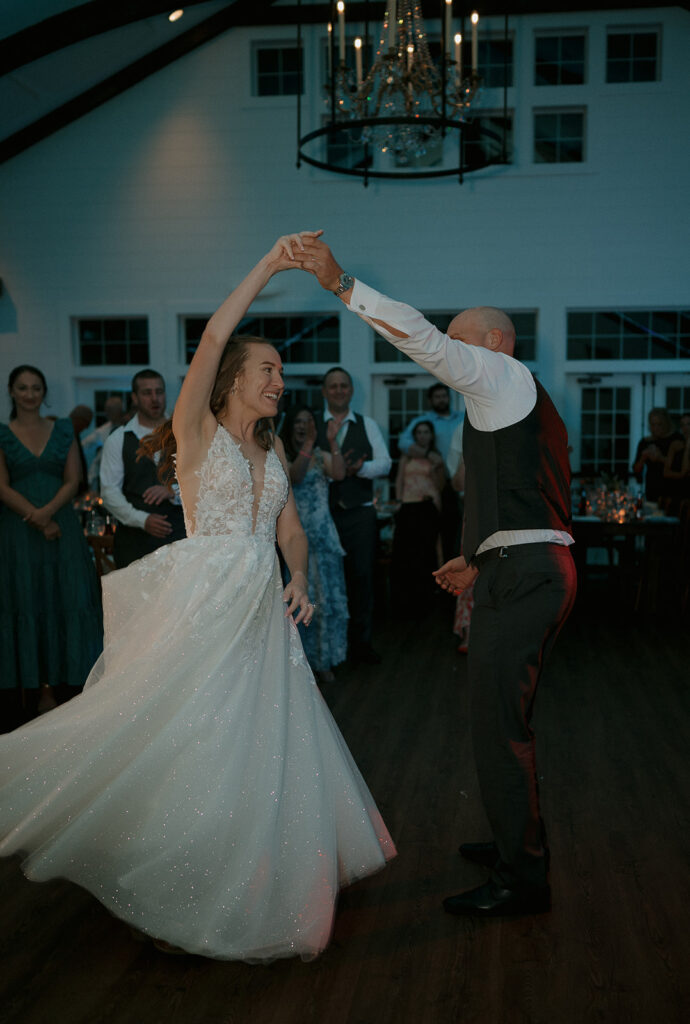Bride and groom sharing a joyful first dance under chandelier in the barn at The Inn at Millrace Pond wedding reception.