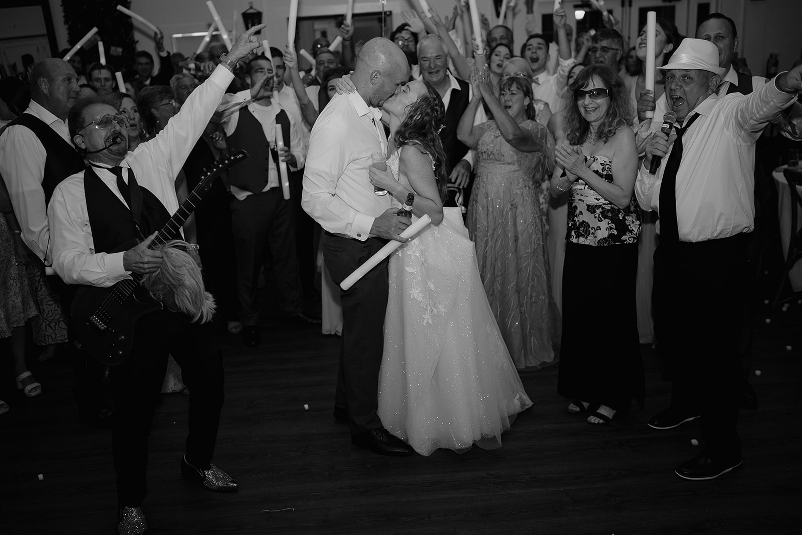 Black and white photo of a bride and groom kissing while surrounded by their guests