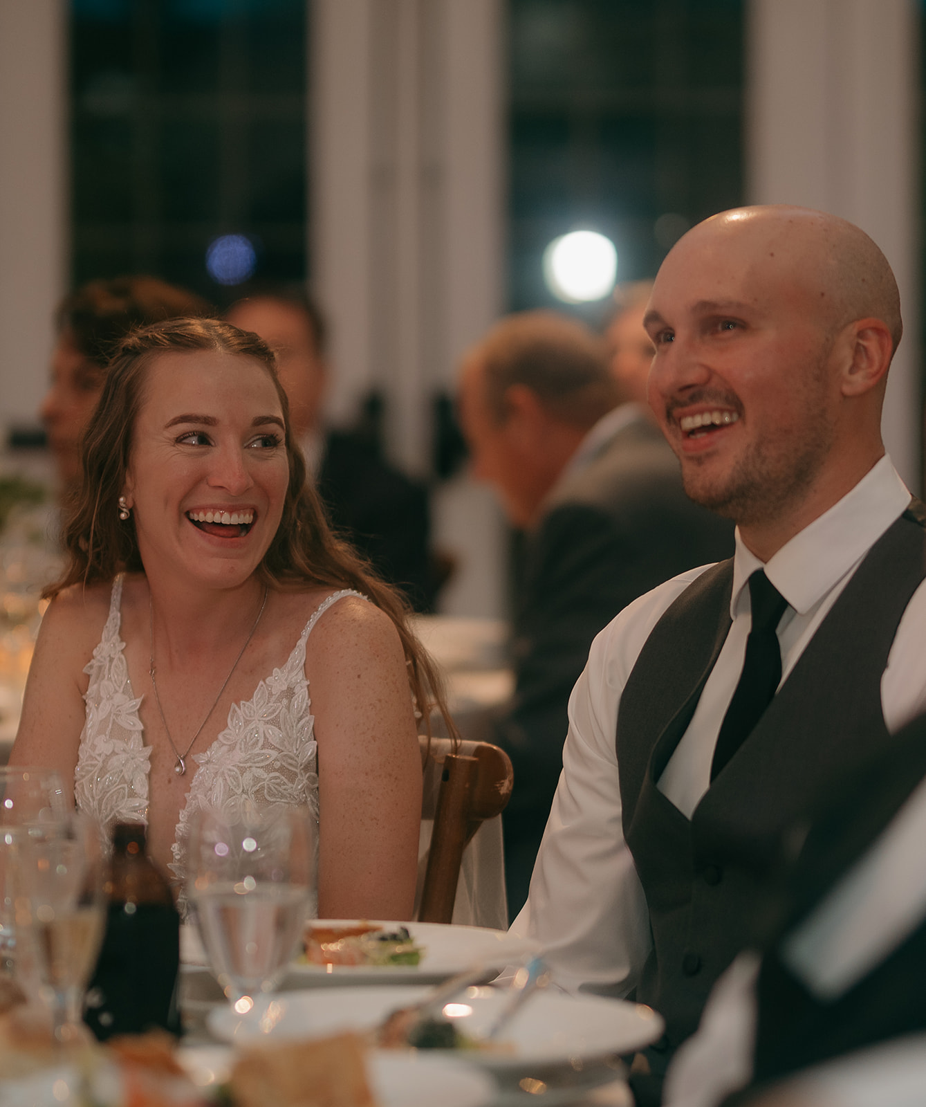 Bride and groom laughing together while seated at reception table, enjoying speeches at The Inn at Millrace Pond wedding reception.