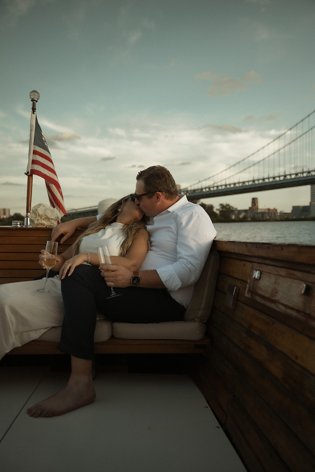 Couple sharing a kiss with champagne glasses on The Argonaut during their dreamy engagement photos in Philadelphia.