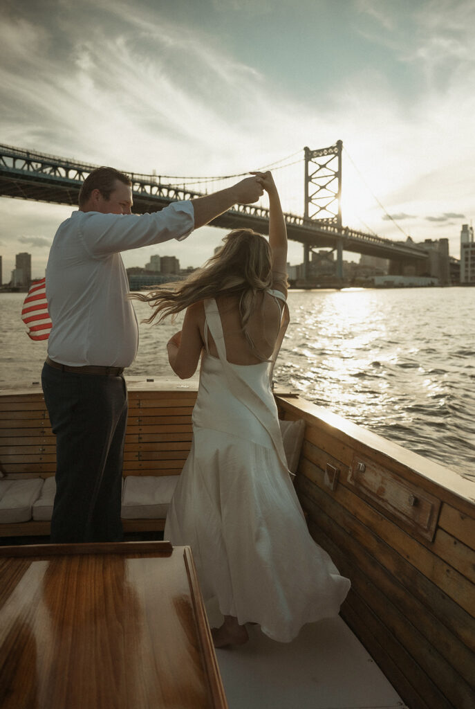 Couple dancing on the boat at sunset with the Ben Franklin Bridge in the background during engagement photos in Philadelphia.