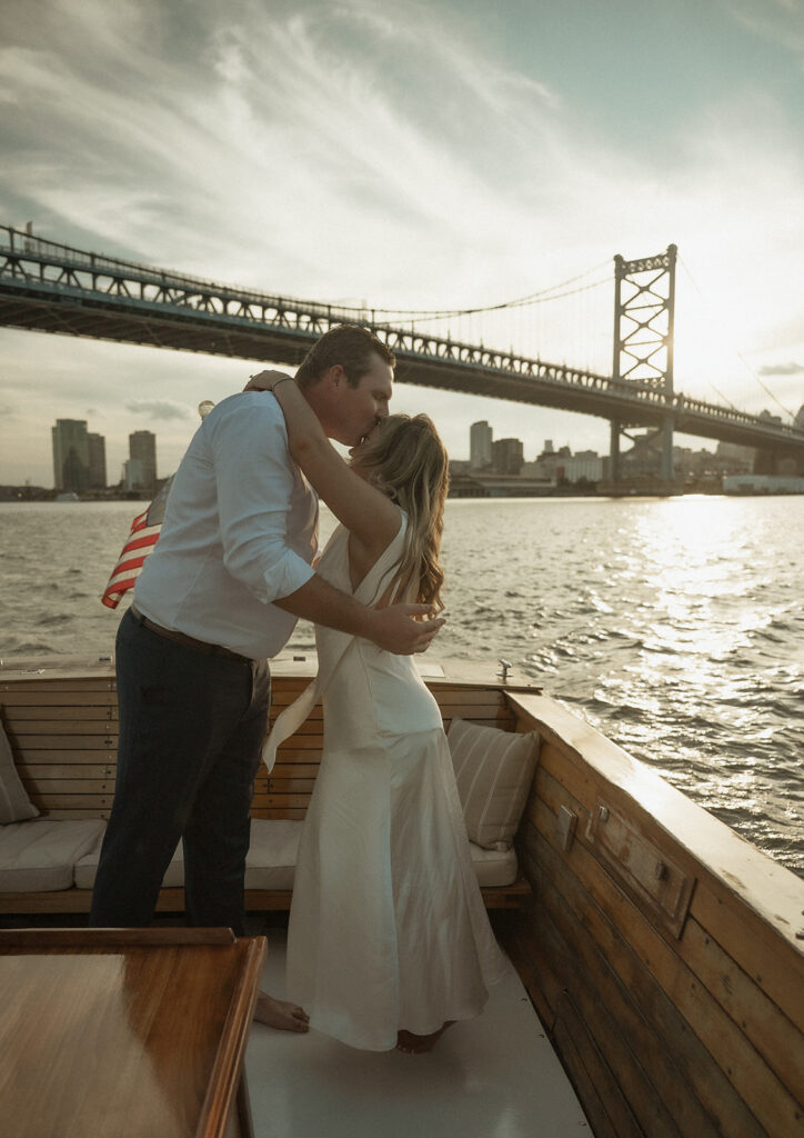 Man kissing his fiancés forehead during their sunset boat engagement photos in Philly