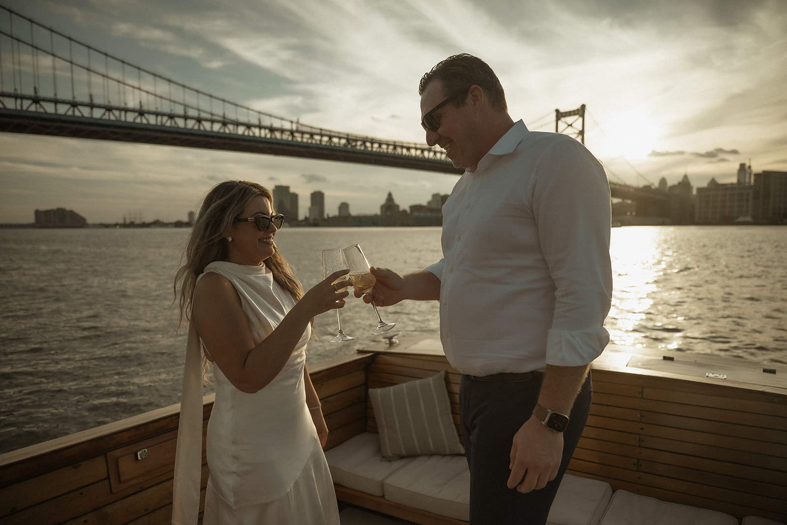 Nicole and Chris clinking champagne glasses on The Argonaut during their dreamy engagement photos in Philadelphia.