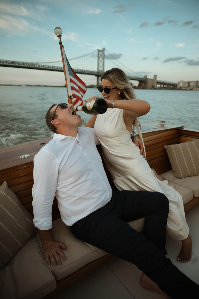 Playful photo of Nicole pouring champagne for Chris on the boat during their engagement photos in Philadelphia.