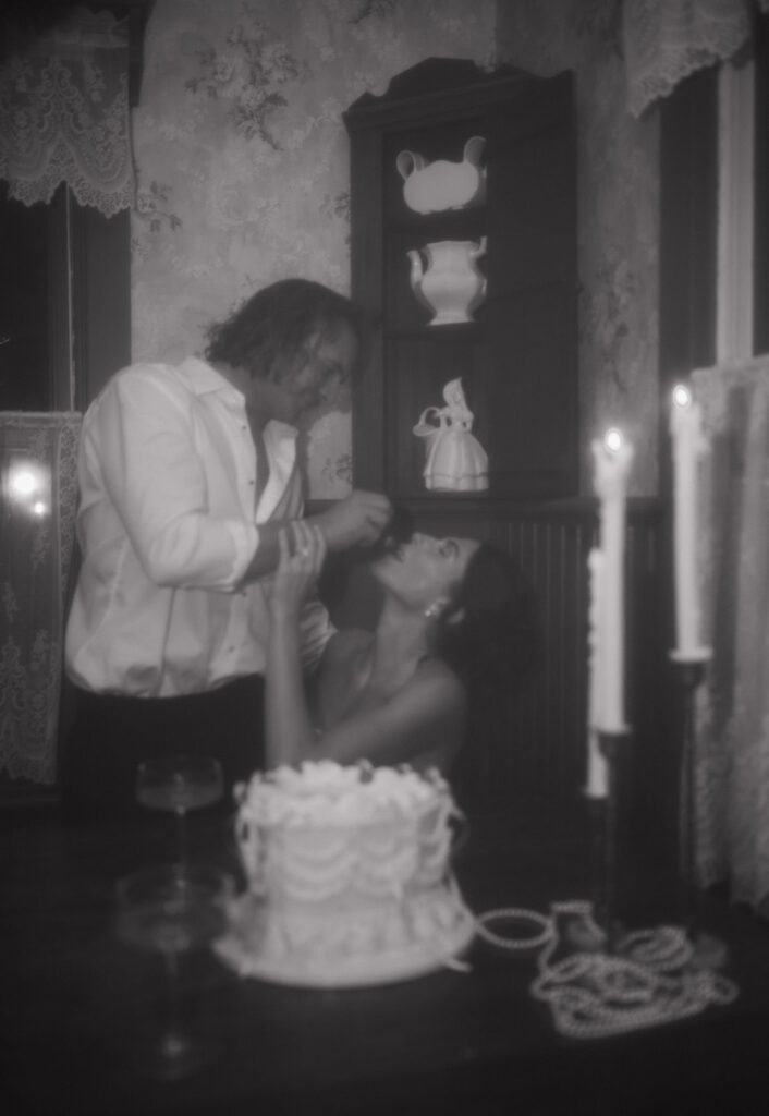 Hazy, dreamy image of the groom feeding the bride cake beside glowing candles during their late-night intimate wedding session.
