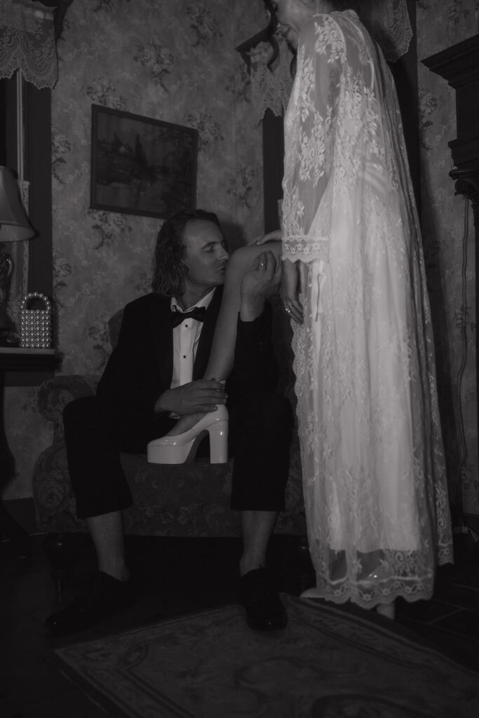 The groom gently kisses the bride’s knee as she stands in a lace robe, creating a tender, emotive moment captured by New Jersey wedding photographer Ell Peters.