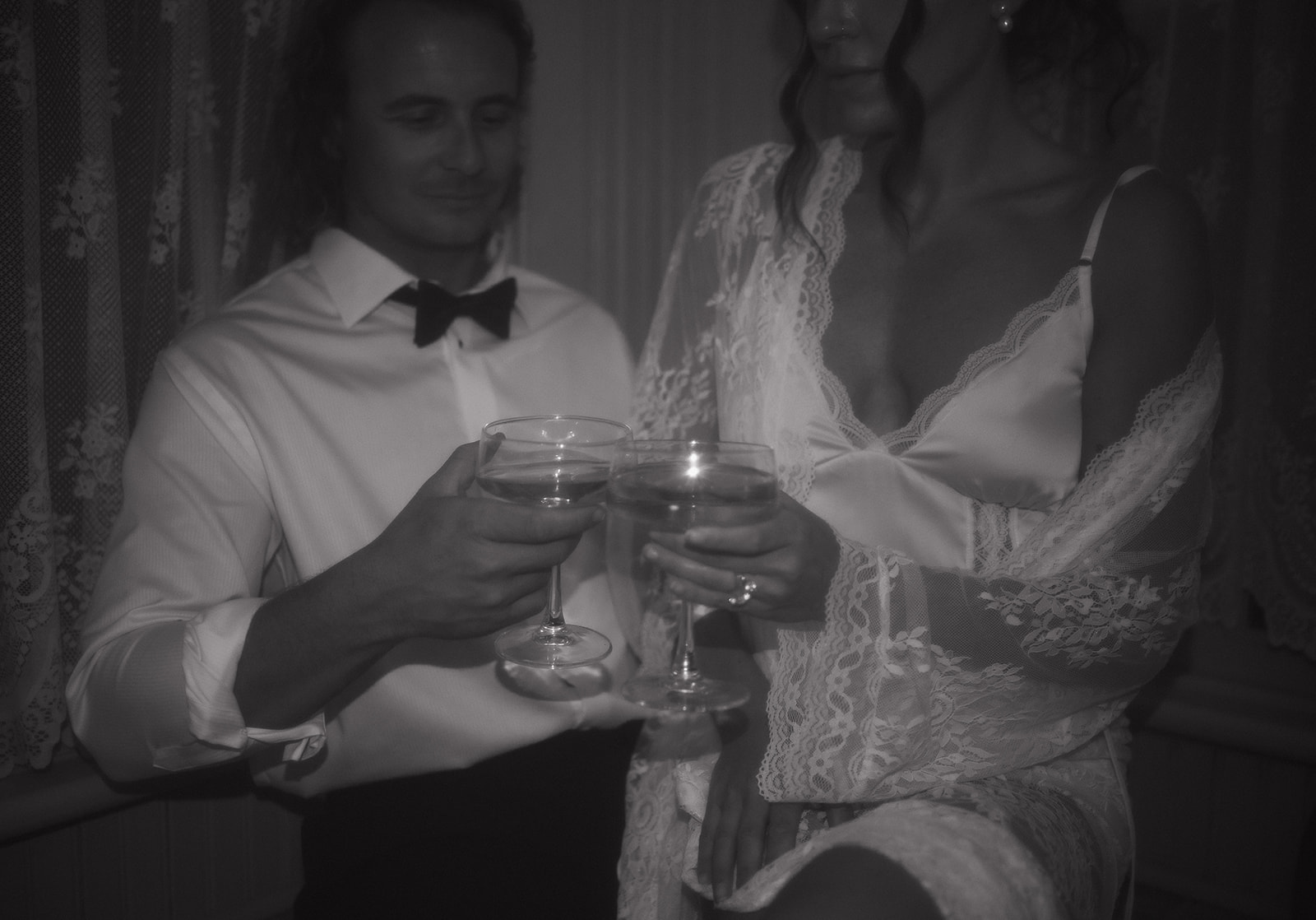 A close-up black-and-white image of the couple clinking glasses in lace and satin, highlighting the quiet romance of their intimate late-night wedding session.