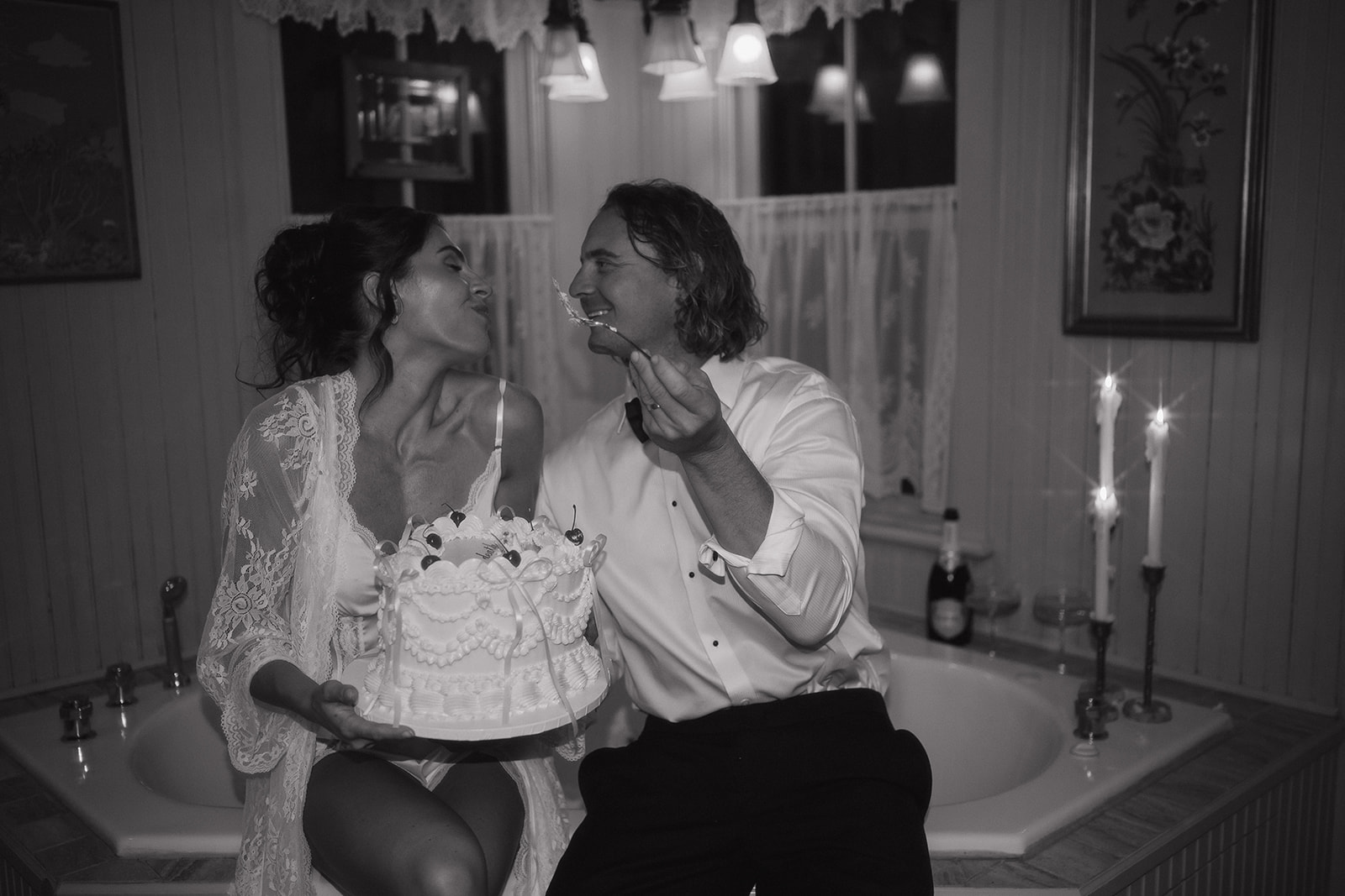 Couple sitting on the edge of a vintage bathtub sharing their wedding cake, leaning in for a kiss during their late-night intimate wedding photos in Frenchtown, NJ.
