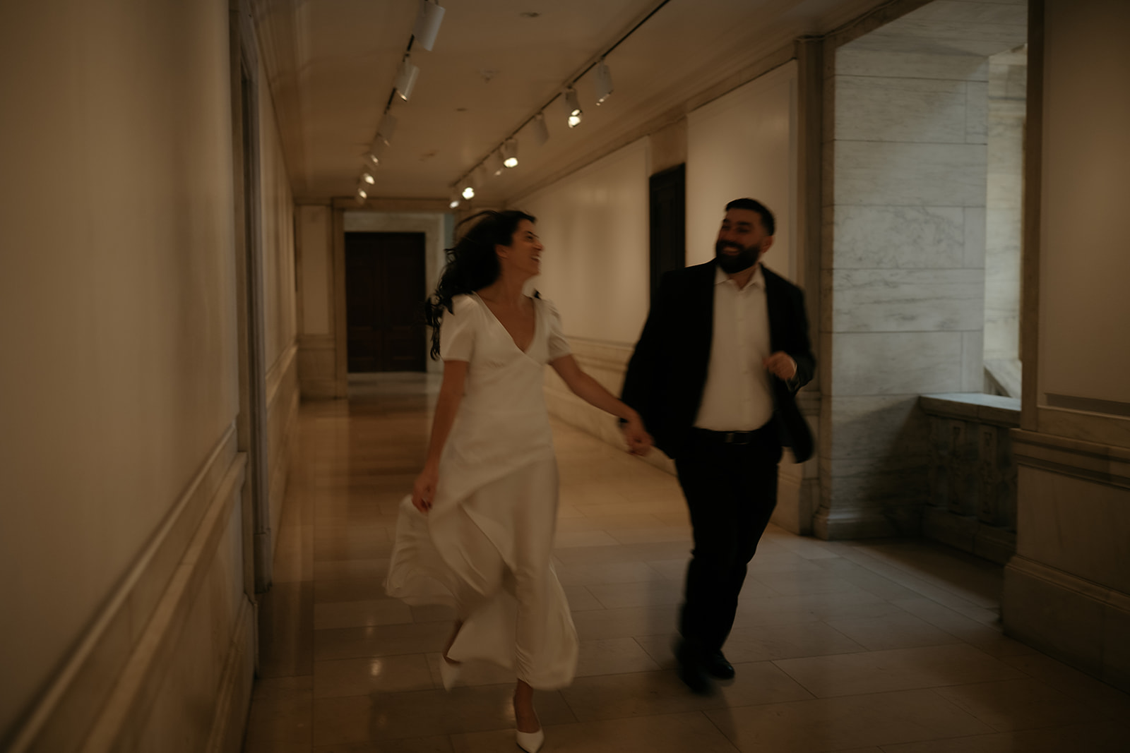 Cinematic engagement photo of a couple running through the halls at the New York Public Library.