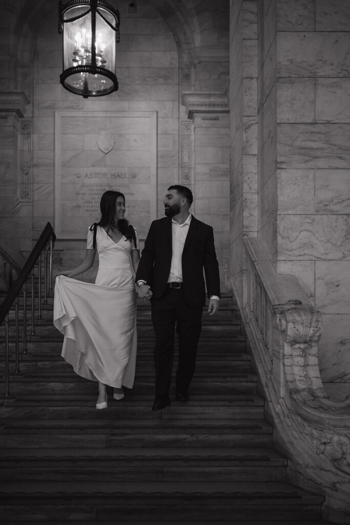 Black and white photo of a couple walking down the staircase at NY Public Library. 