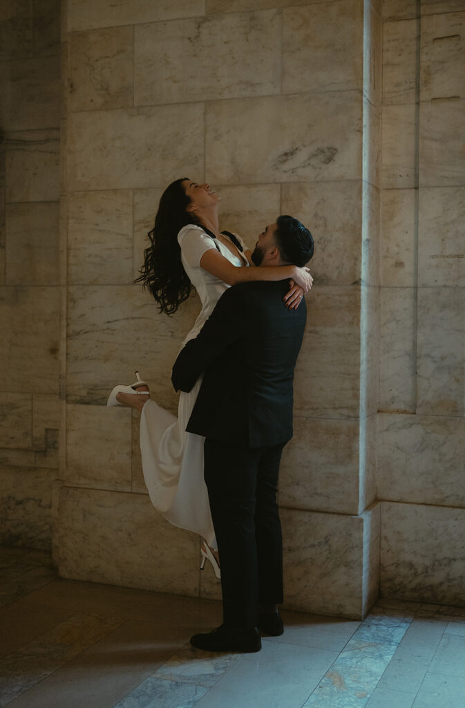 Man picking up his fiancé as she smiles during their engagement session. 