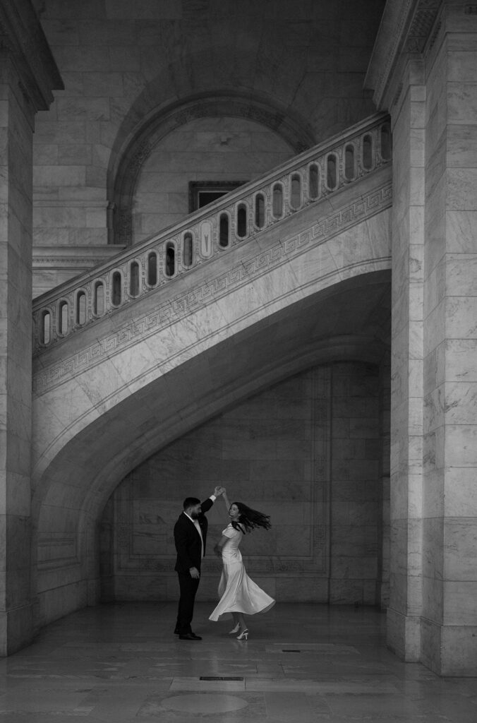 Black and white photo of a man twirling his fiancé during their New York Public Library engagement photos.