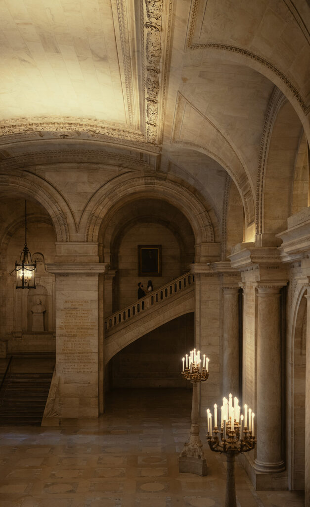 Photo from afar of a couple walking up the stairs for their New York Public Library engagement photos.