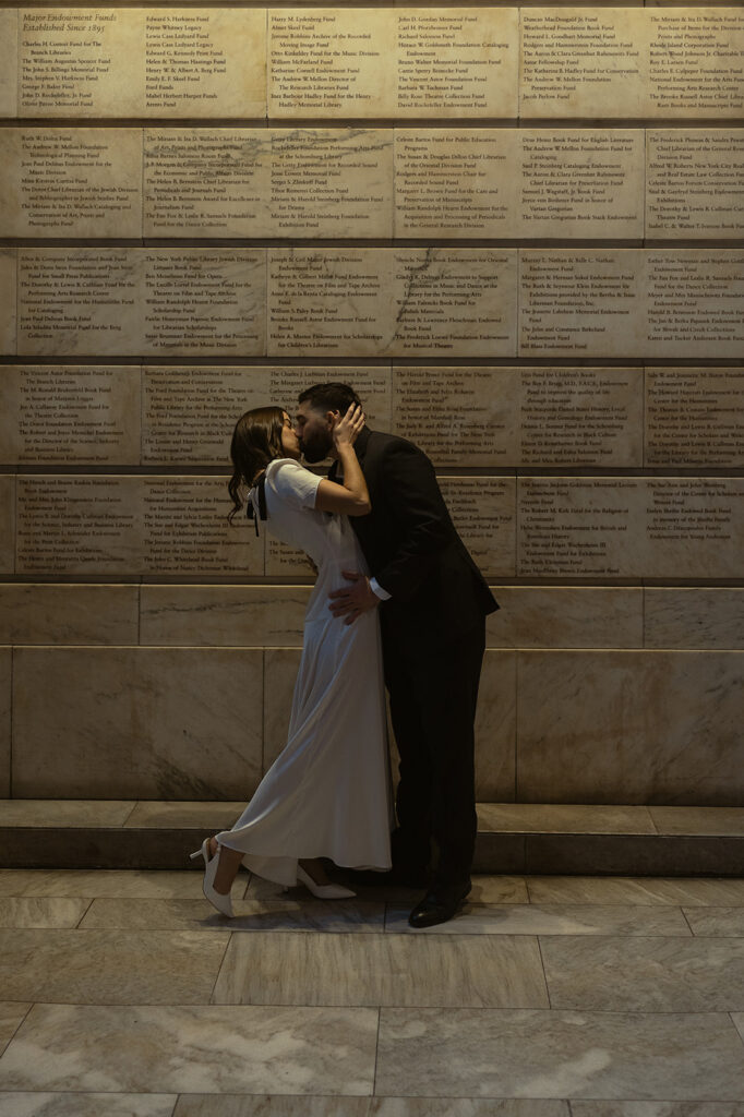 Couple kissing in front of a wall with writing for their NY Public Library engagement photos.