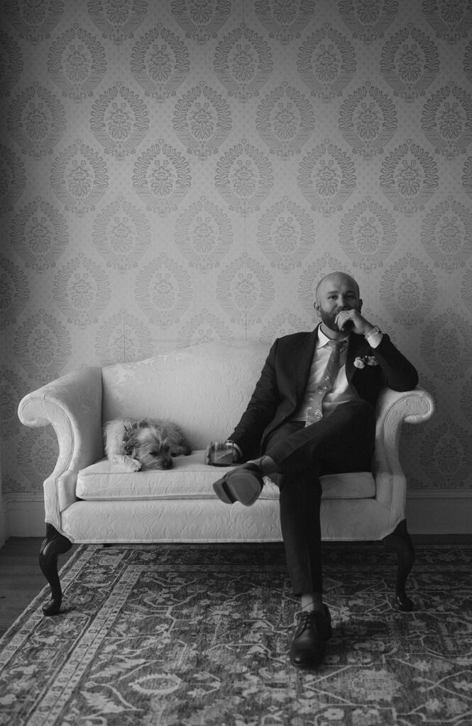 Groom sitting on a couch with his dog. 