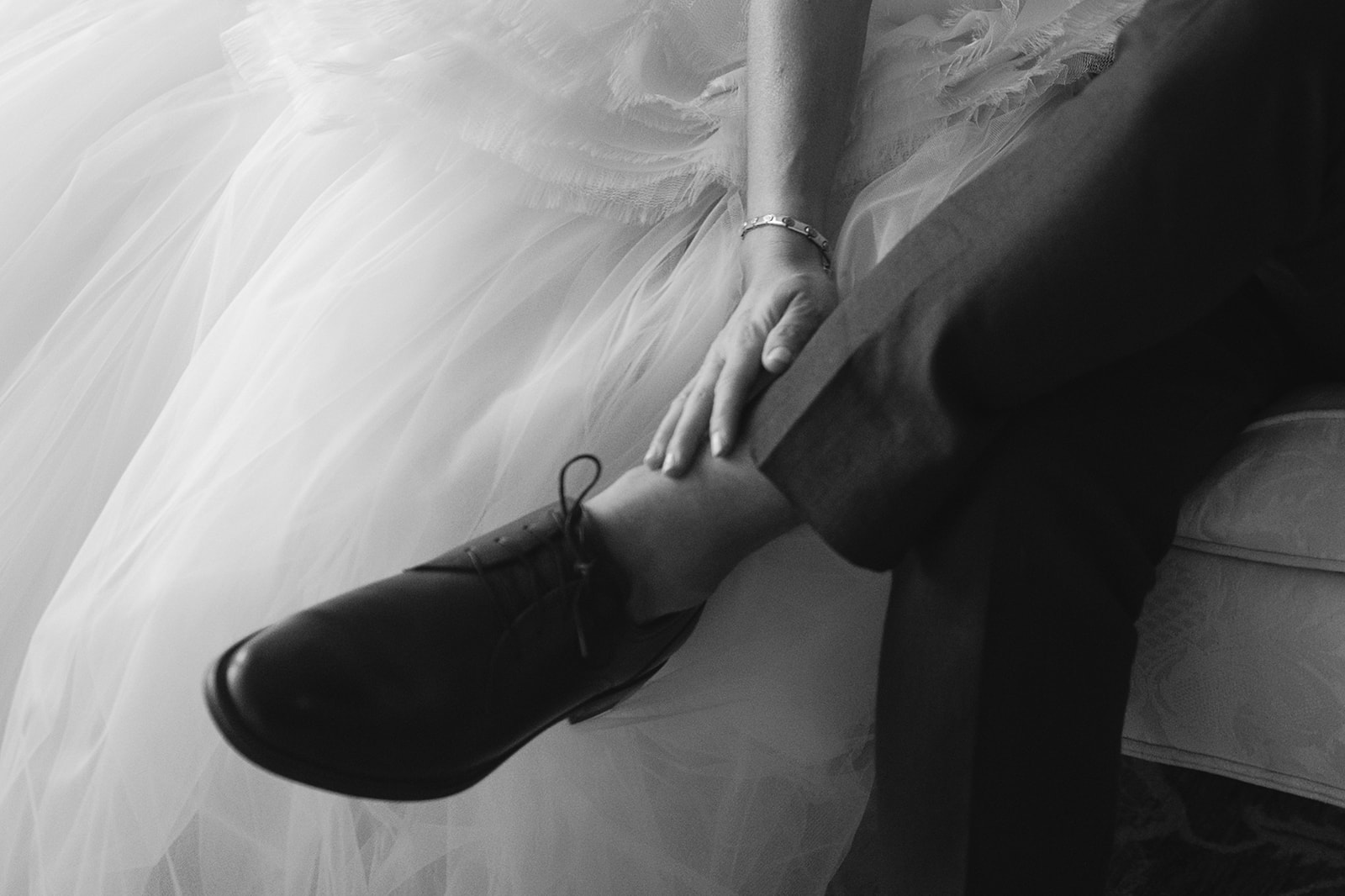 Black and white photo of a bride caressing her grooms leg.