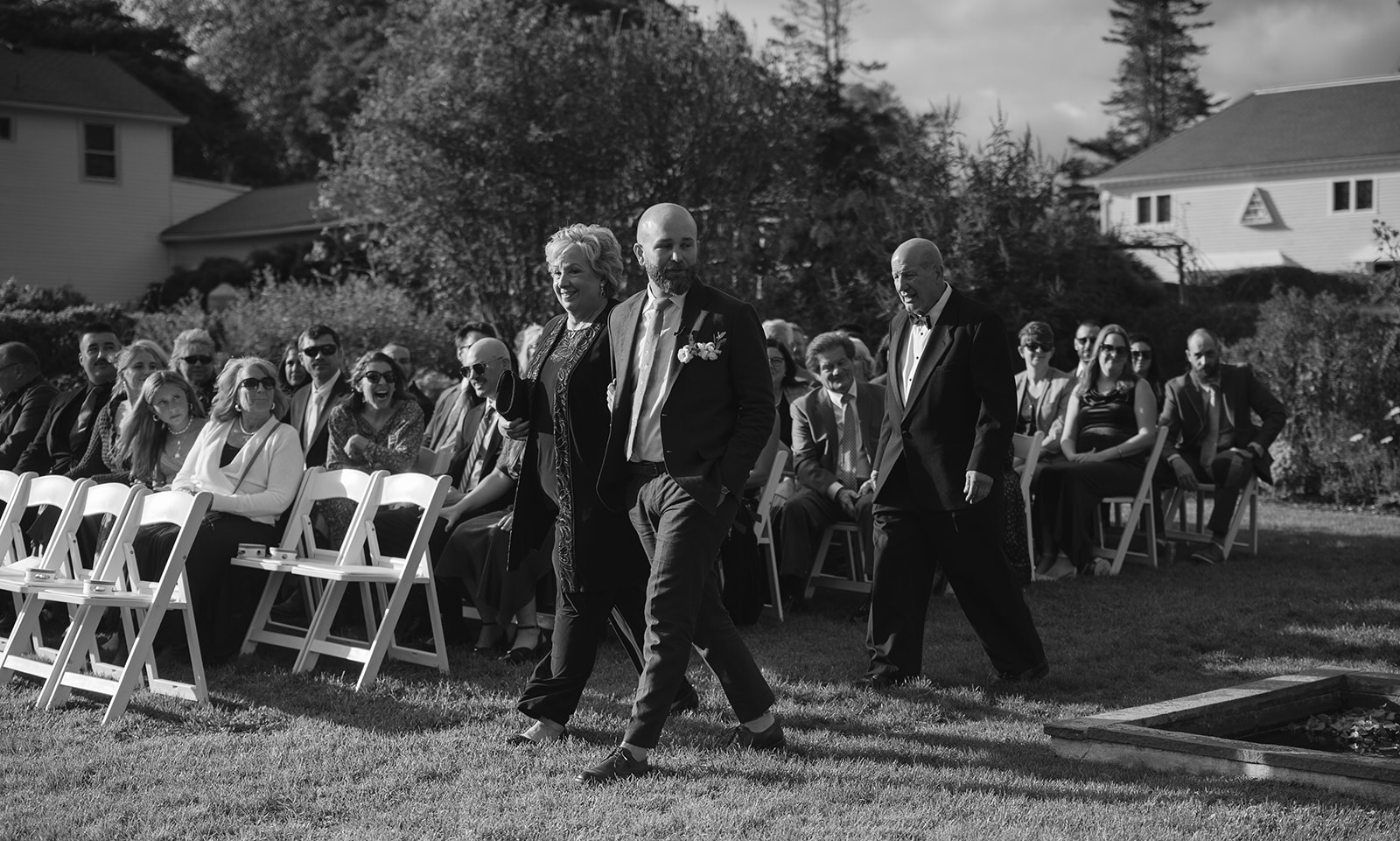 Groom walking down aisle with parents during outdoor ceremony in Boxwood Garden at Stone Acres Farm wedding in Connecticut.