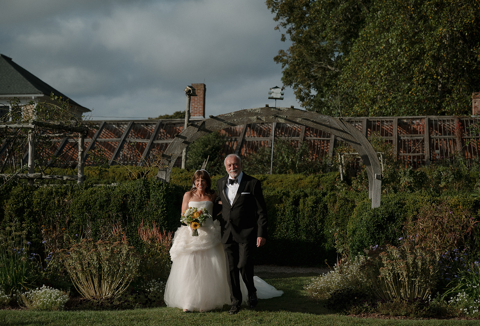 Bride walking down garden aisle with father during Boxwood Garden ceremony at Stone Acres Farm.