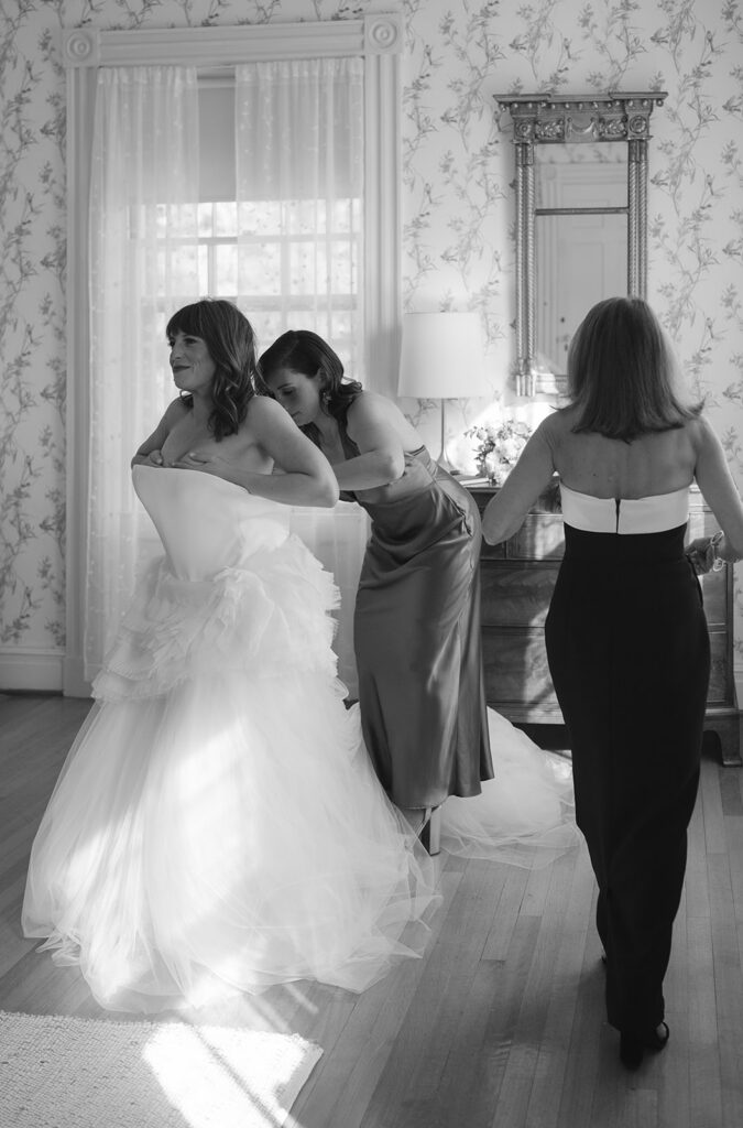 Black and white photo of a bride being helped into her Vera Wang wedding dress in Manor House at Stone Acres Farm in Stonington, CT.