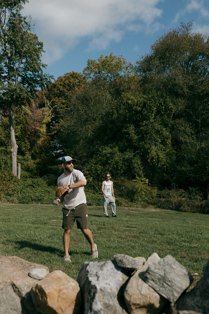 Groomsmen playing baseball outdoors on lawn during relaxed morning of Stone Acres Farm wedding.