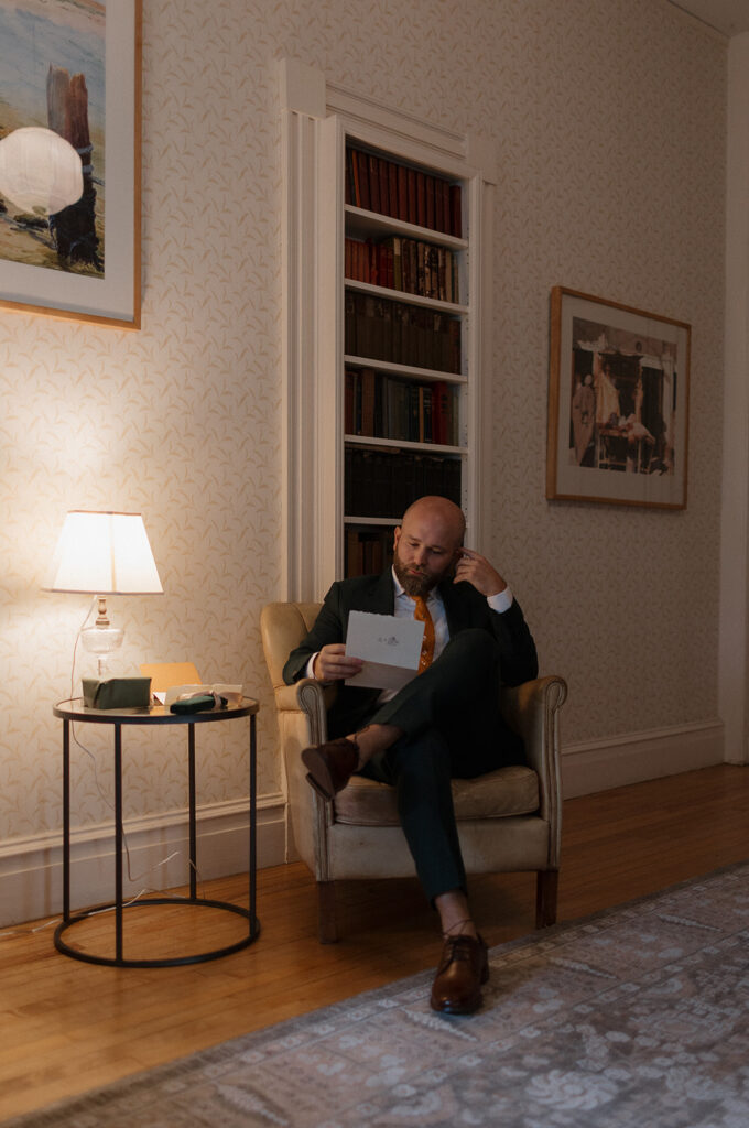 Groom reading a letter while seated in cozy getting ready space at Stone Acres Farm wedding venue.