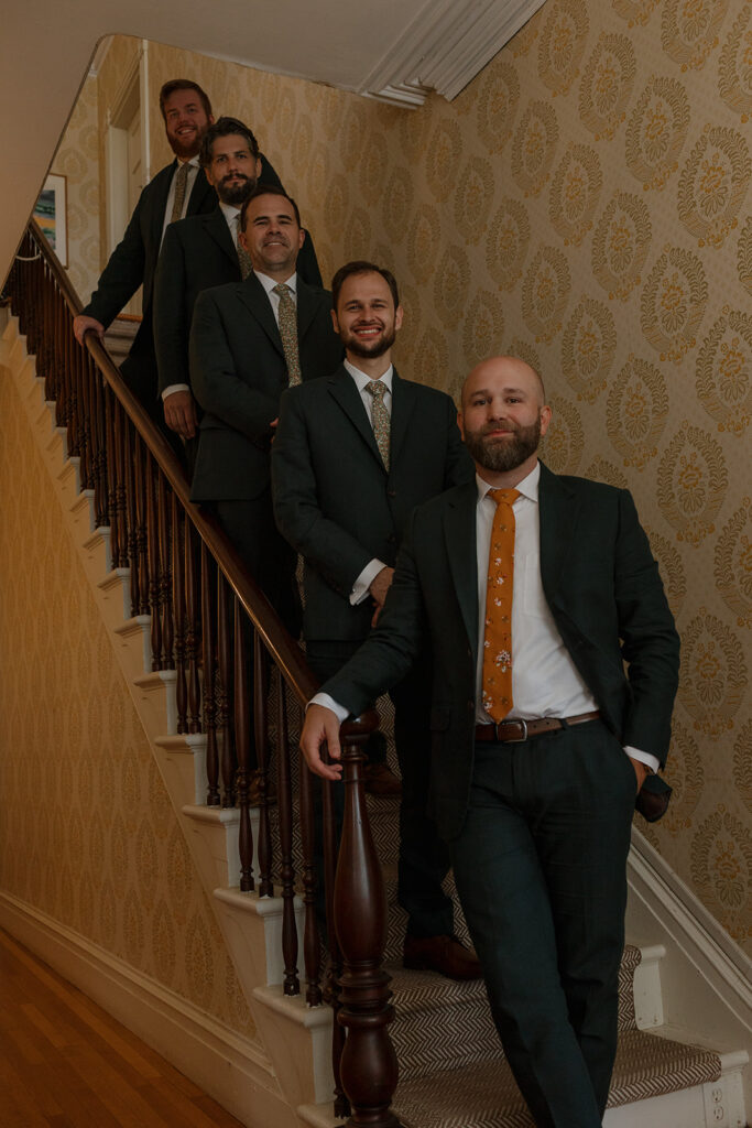 Groom and groomsmen walking down staircase in suits at Stone Acres Farm wedding getting ready location.