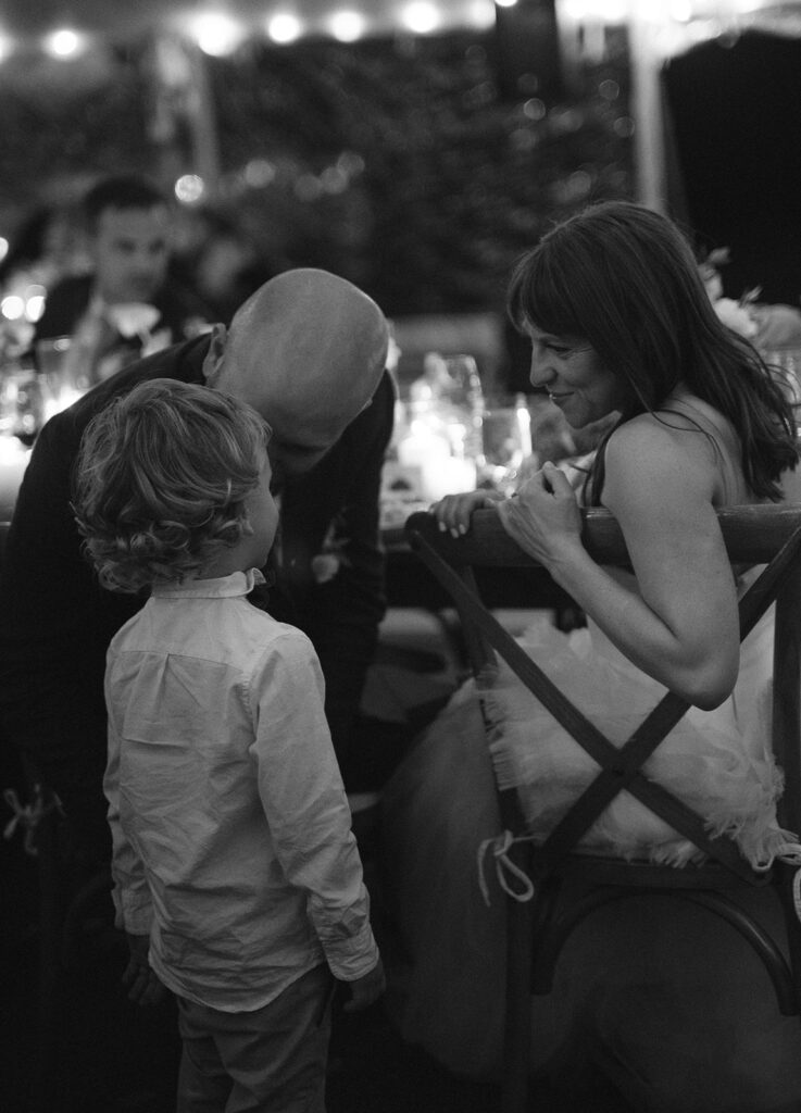 Candid black and white photo of a bride and groom talkingwith a little boy. 