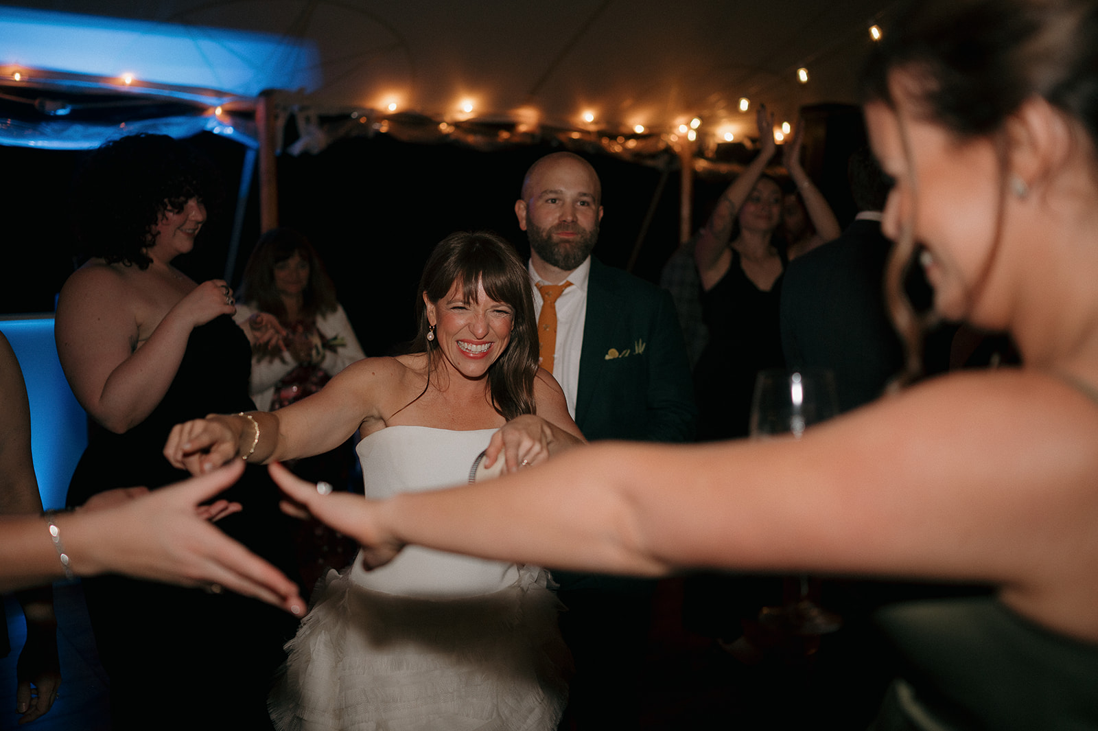 Groom watching bride dance with friends during joyful tented reception celebration at Stone Acres Farm.