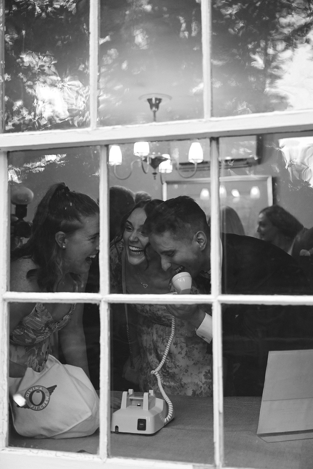 Black and white cinematic style wedding photo of guests leaving a message on a vintage style phone during the reception.