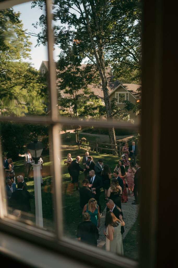 Cinematic wedding photo of guests mingling during cocktail hour through the window.