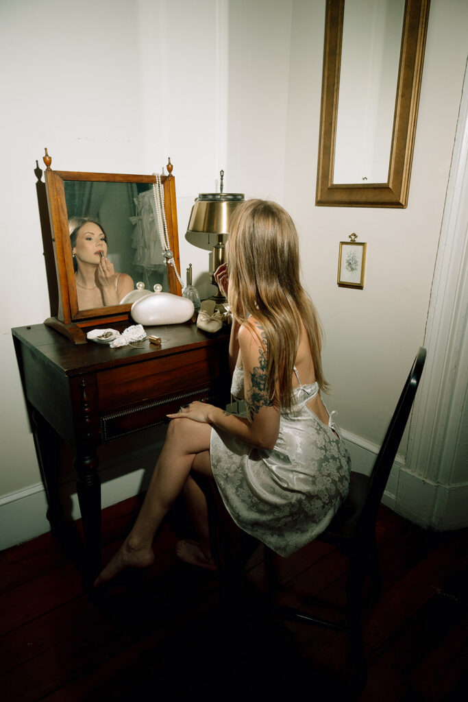 Flash photo of a bride applying her lipstick in the mirror during her getting ready wedding photos at Vaux Studio in Philadelphia.