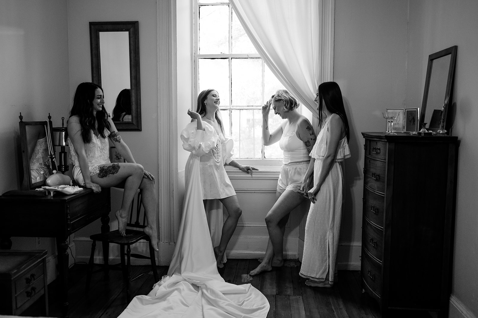 Black and white photo of a bride and bridesmaids posing by a window for getting ready wedding photos at Vaux Studio in Philadelphia. 